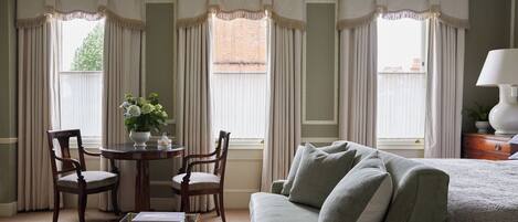 A room with a green sofa, two wooden chairs, a glass coffee table, and a small table with a vase of flowers.