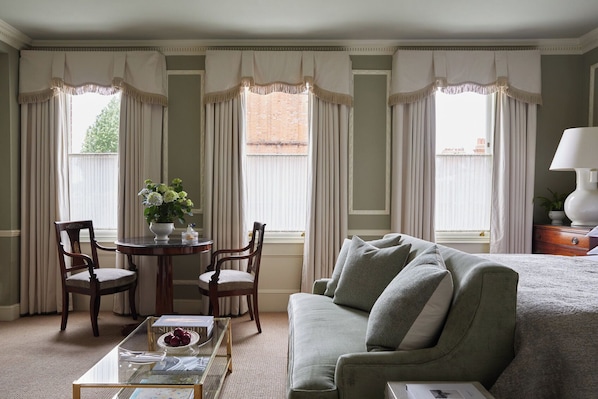 A room with a green sofa, two wooden chairs, a glass coffee table, and a small table with a vase of flowers. - The Egerton House Hotel (London)