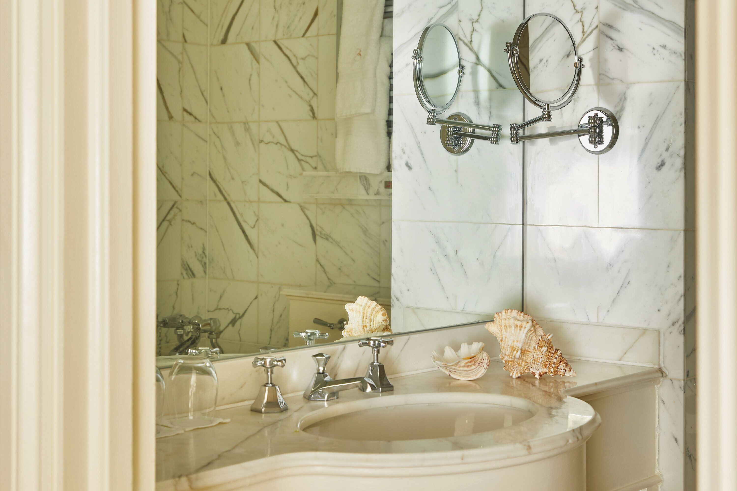 A bathroom with a marble sink, two mirrors, and a decorative shell.