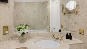 A bathroom with a marble sink, a mirror, a bathtub, and a vase of flowers.