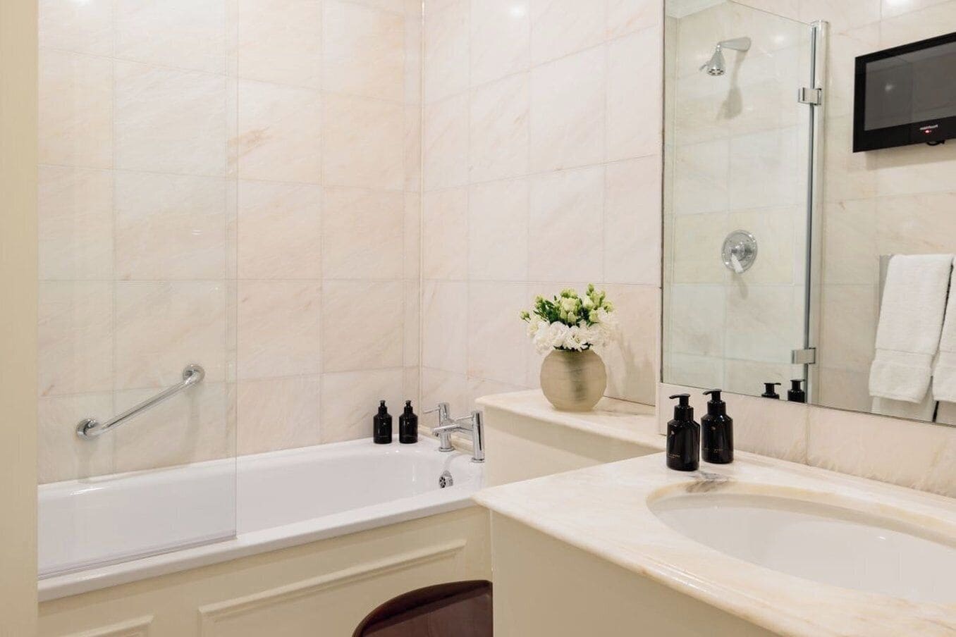 A modern bathroom with a bathtub, two sinks, a vanity, a mirror, and a shower.