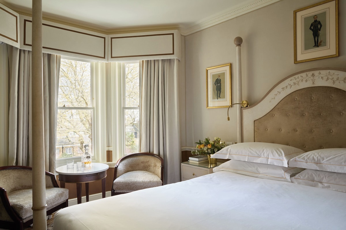 A hotel room with a large bed, a round table, two chairs, a nightstand, and a window with curtains.