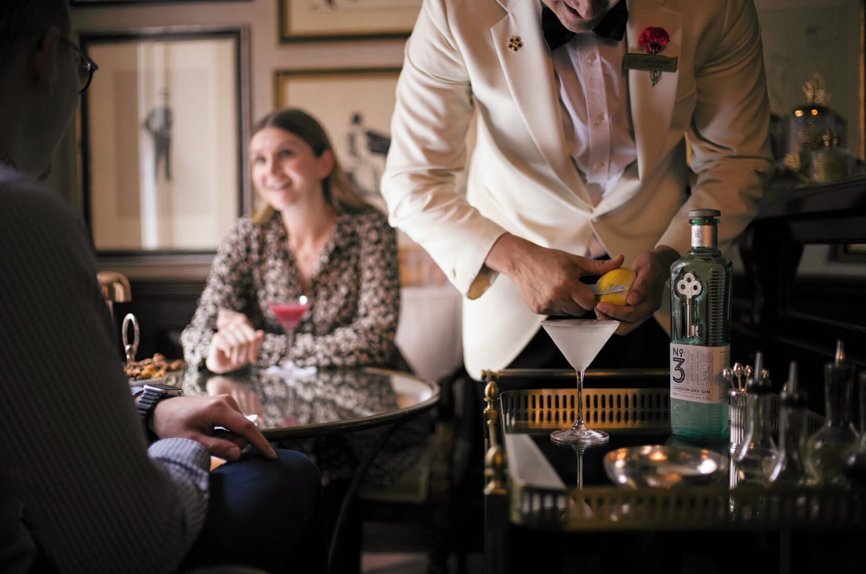 A bar setting with a bartender preparing a drink, a seated woman with a martini, and a man in a suit.