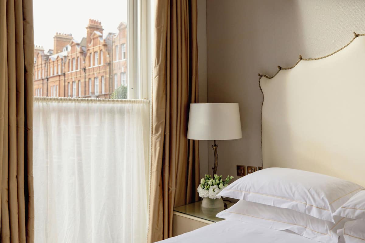 A hotel room with a bed, a bedside table with a lamp, and a window with curtains.