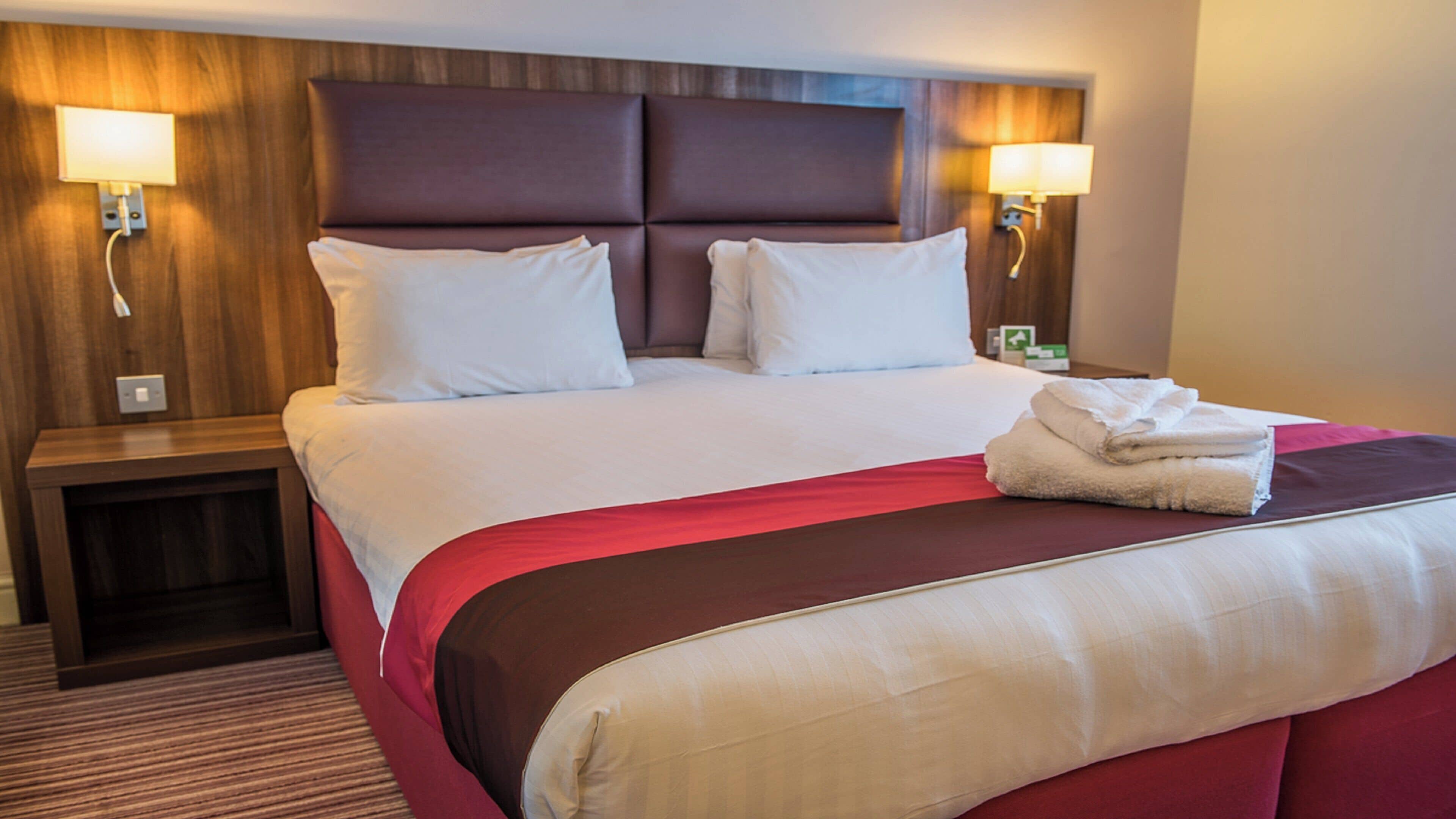 A hotel room with a large bed, two bedside lamps, and a neatly made bed with a folded towel.