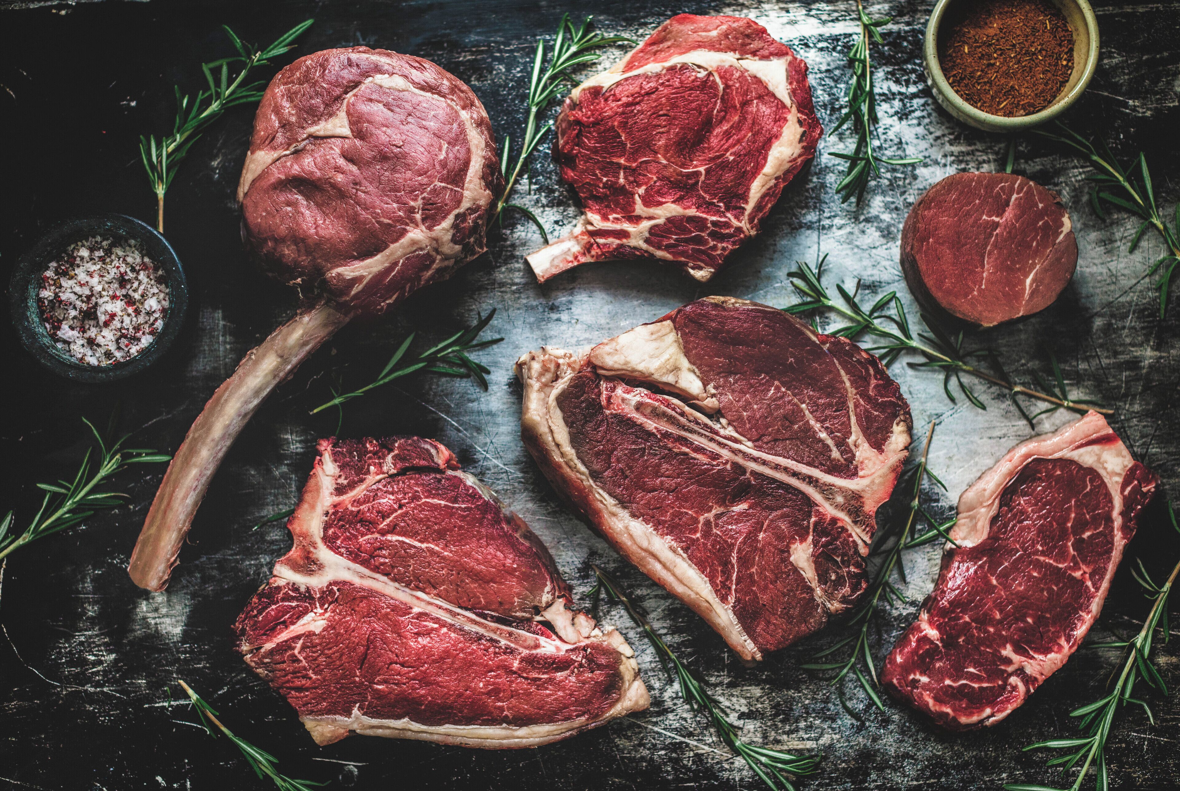 Raw lamb chops with rosemary and coarse salt on a dark wooden surface.