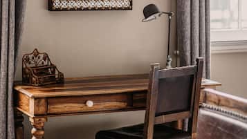 A wooden desk with a lamp, a decorative box, and a chair in a room with a window and curtains.