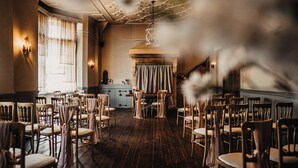 Un salón de banquetes con filas de sillas de madera, una mesa central y una lámpara decorativa colgante.