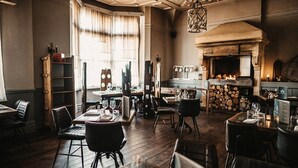 Un restaurante acogedor con suelos de madera, mesas dispuestas para comer y una chimenea al fondo.