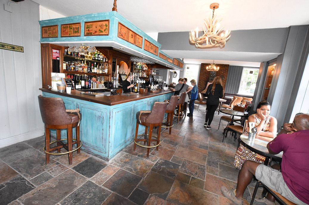A bar area with a blue counter, multiple stools, and a bartender. There are tables and chairs for dining in the background.