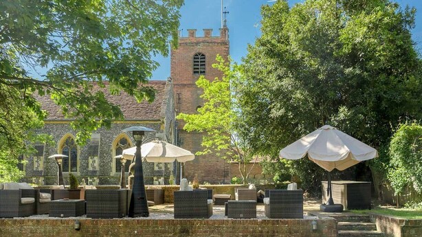 Un patio con mesas al aire libre, un edificio de ladrillo con una torre y un cielo despejado.