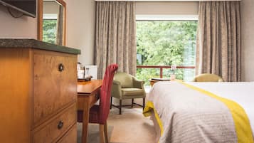 A hotel room with a bed, a wooden dresser, a desk, a chair, and a window with curtains.