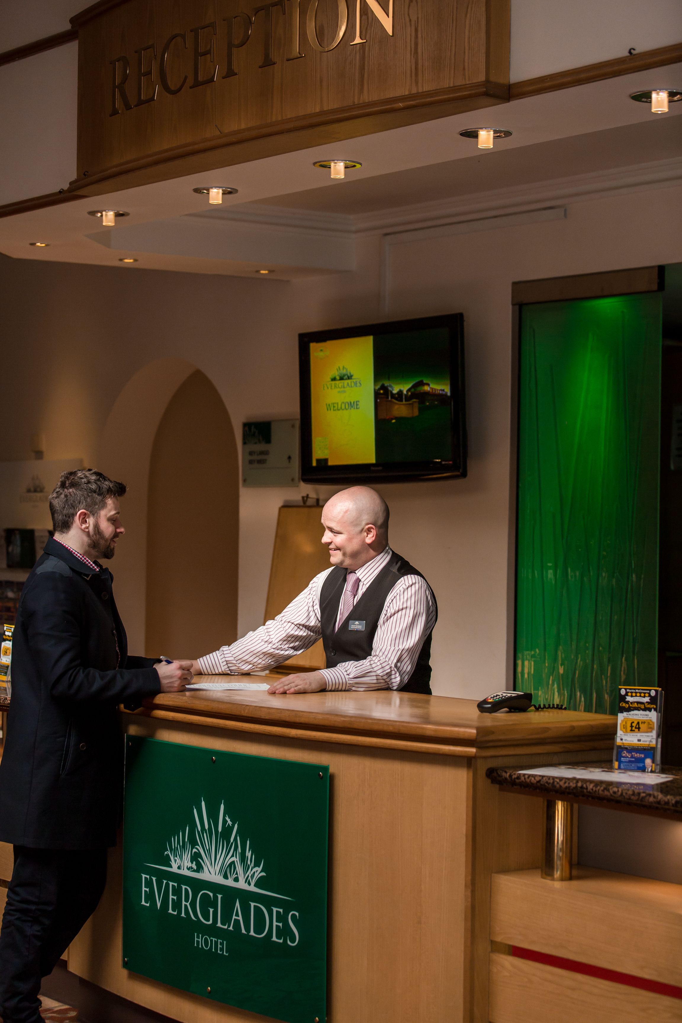 Un comptoir d’accueil à l’hôtel Everglades, avec un espace d’accueil en bois, un écran de télévision et un rideau vert.