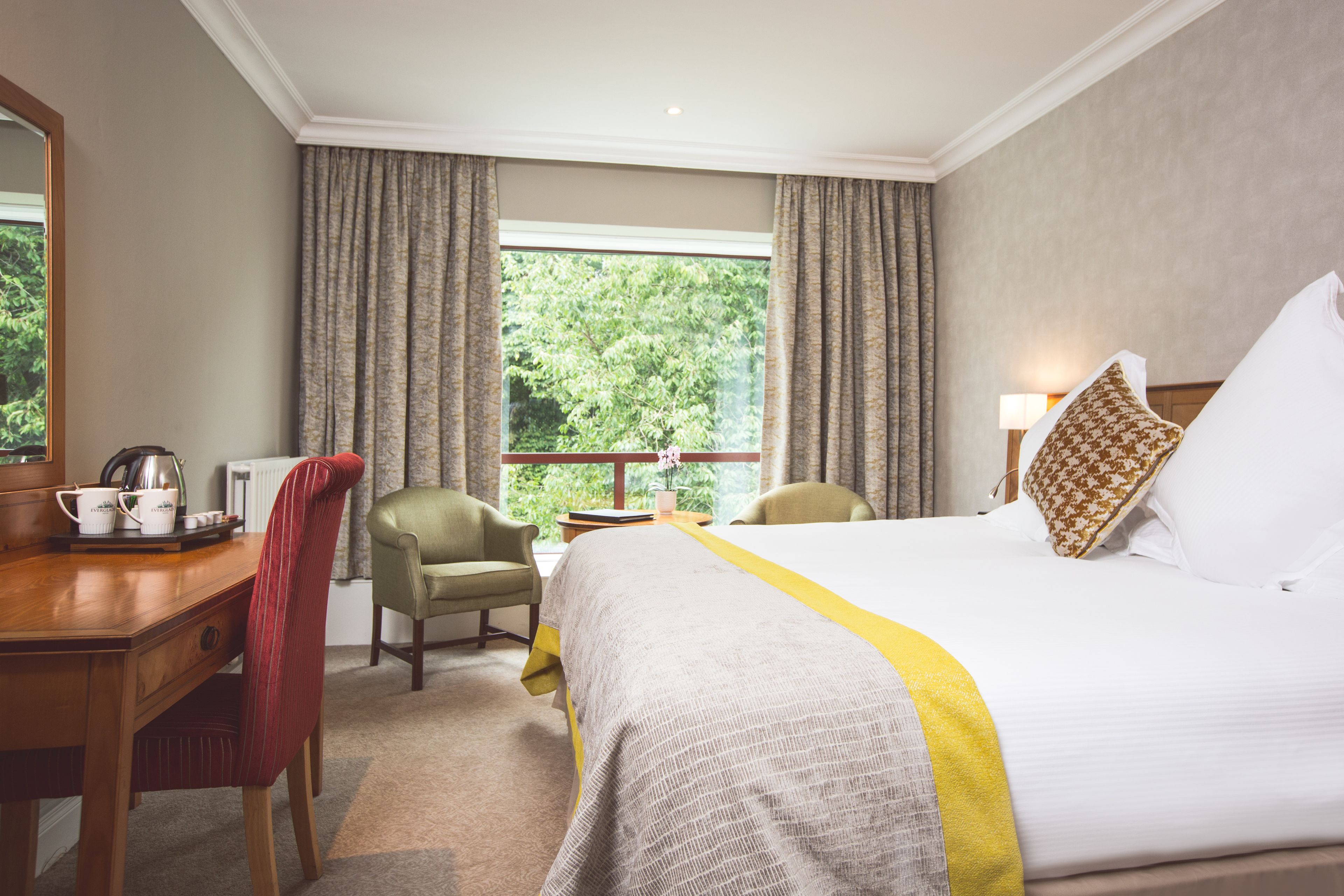 Habitación de hotel con una cama grande, un escritorio con silla, una ventana con cortinas y vistas a zonas verdes.