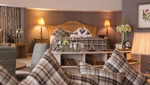 A hotel room with a bed, two bedside lamps, a nightstand, a small table with a vase of flowers, and a couch with plaid cushions. - Everglades Hotel (Londonderry)