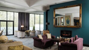 A spacious living room with large windows, a fireplace, and a large mirror on the wall. - Everglades Hotel (Londonderry)