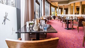 A restaurant with tables set for dining, large windows, and a carpeted floor. - Everglades Hotel (Londonderry)