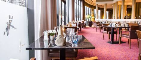 A restaurant with tables set for dining, large windows, and a carpeted floor.