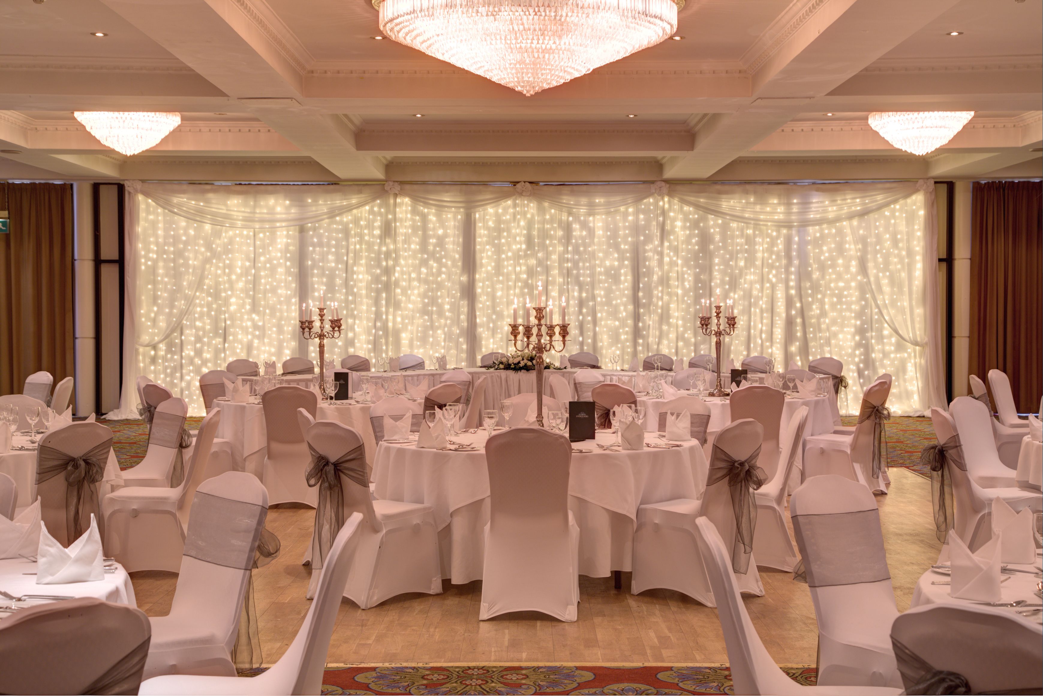 A banquet hall with round tables, white tablecloths, and chairs with grey sashes.
