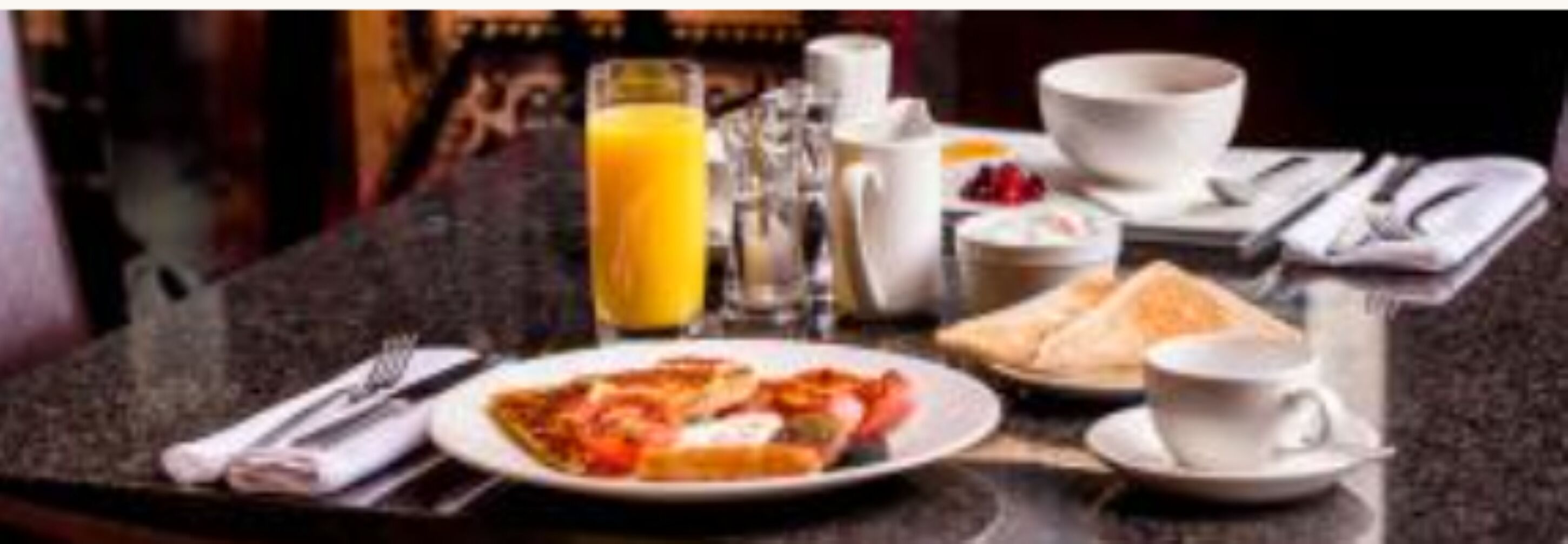 Uma mesa de café da manhã com um prato de comida, um copo de suco de laranja, uma xícara de café e um sanduíche.