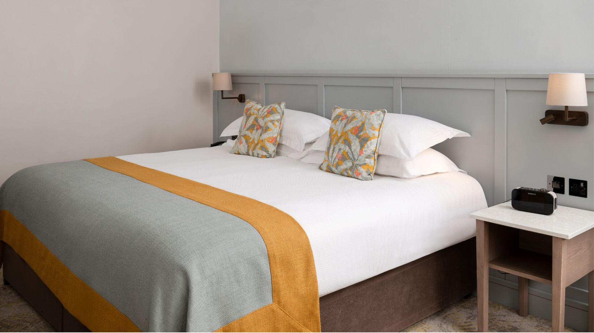 A hotel room with a large bed, a bedside table with a lamp, and a small desk with a radio.