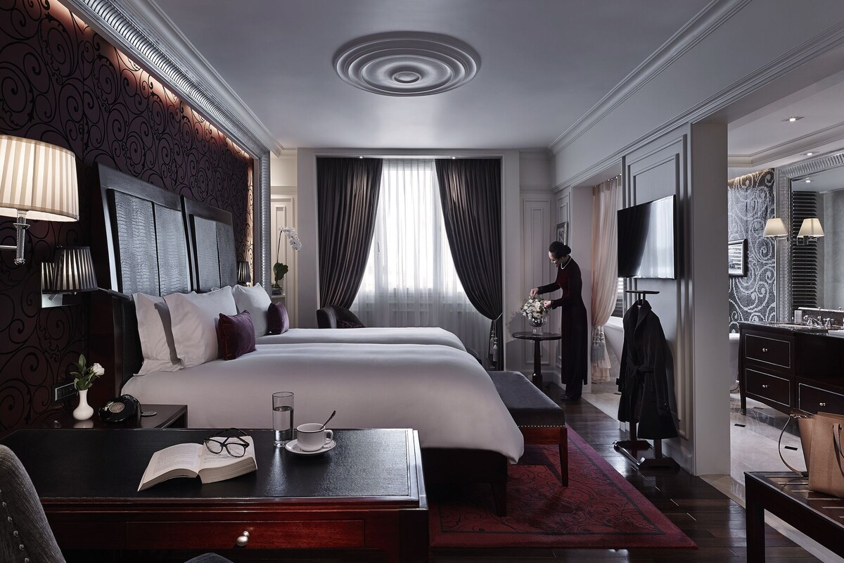 Ein Hotelzimmer mit einem großen Bett, Nachttischen, einem Schreibtisch mit Stuhl, einem Fernseher und einem durch eine offene Tür einsehbarer Badezimmer.