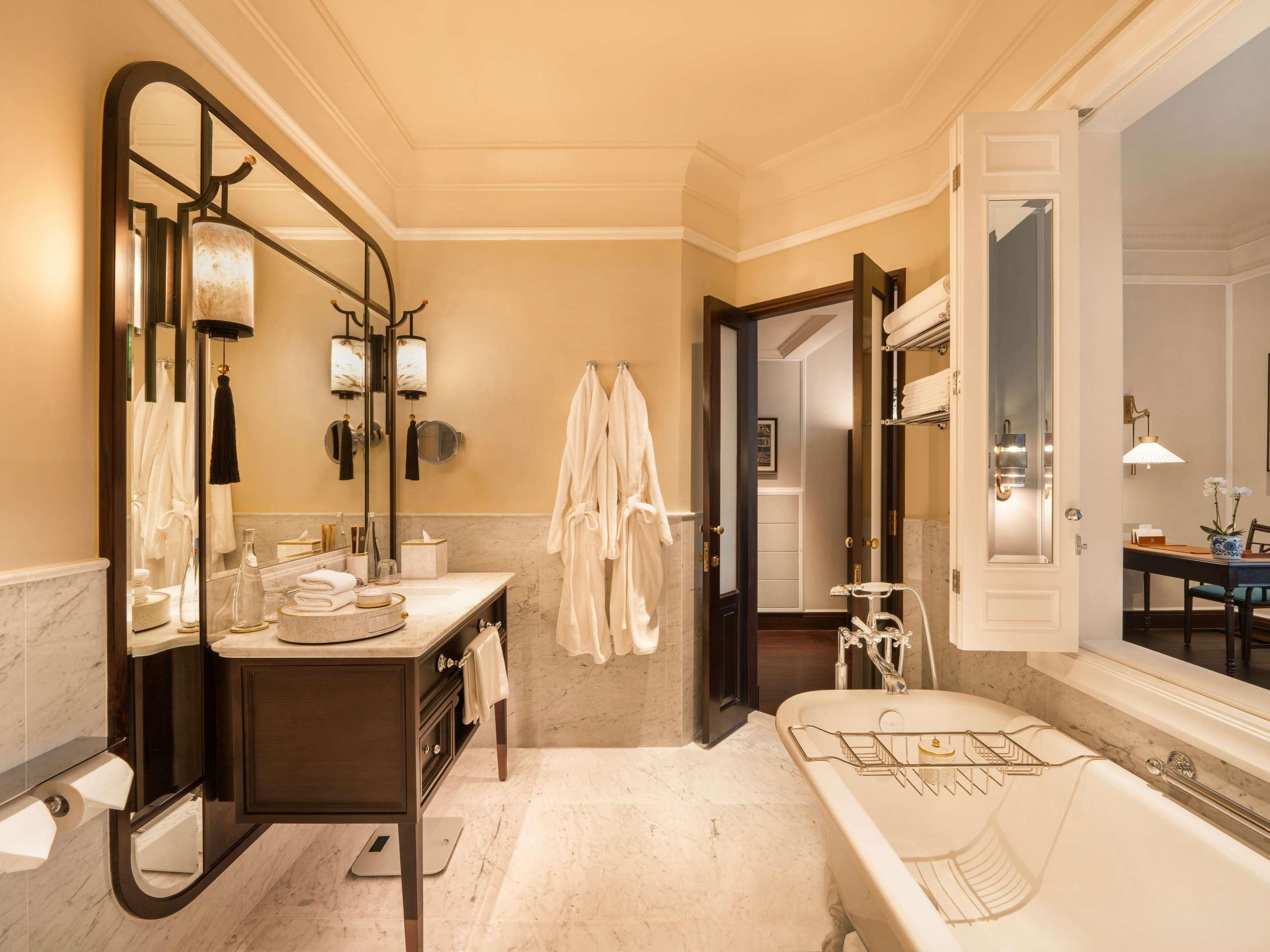 A spacious bathroom with a large mirror, a bathtub, and a vanity with a marble countertop.