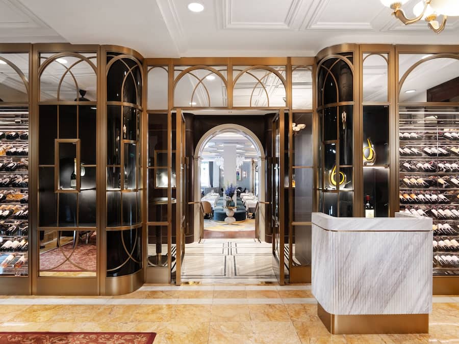 Une cave à vin luxueuse, dotée de nombreuses étagères à façade vitrée, d’un comptoir d’accueil en marbre et d’une grande porte en arc donnant sur une salle à manger.