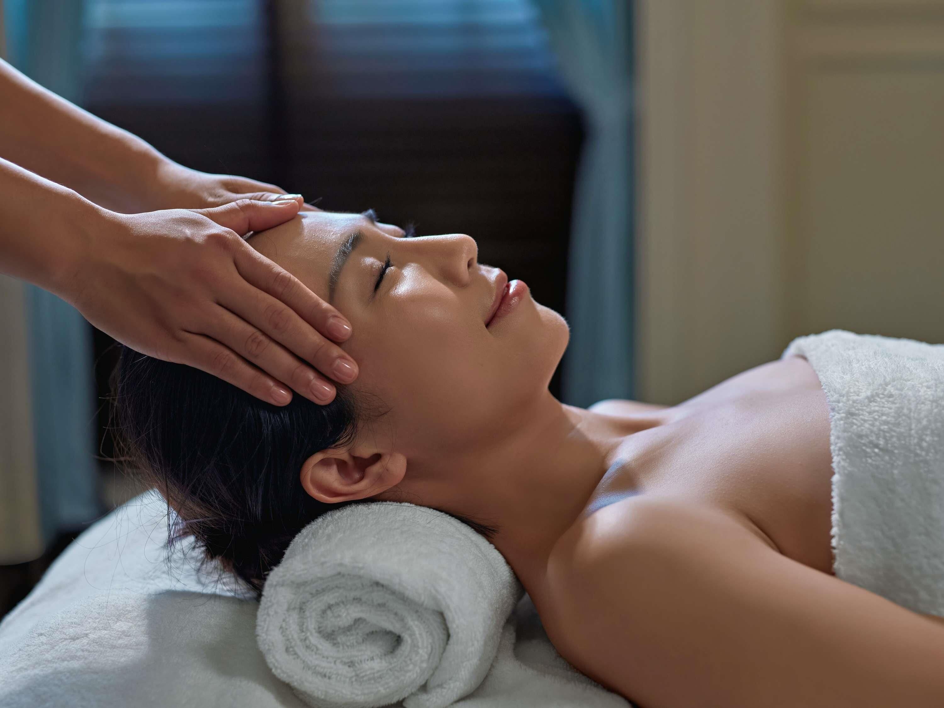 A person receiving a head massage, with a towel and a rolled towel on the side.