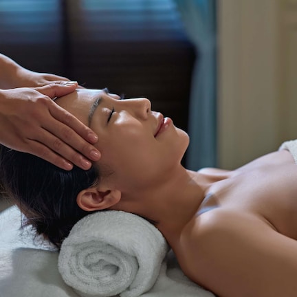 A person receiving a head massage, with a towel and a rolled towel on the side.