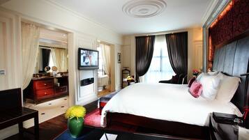 Una habitación de hotel con una cama grande, televisión, escritorio con silla, cómoda y un florero con flores.