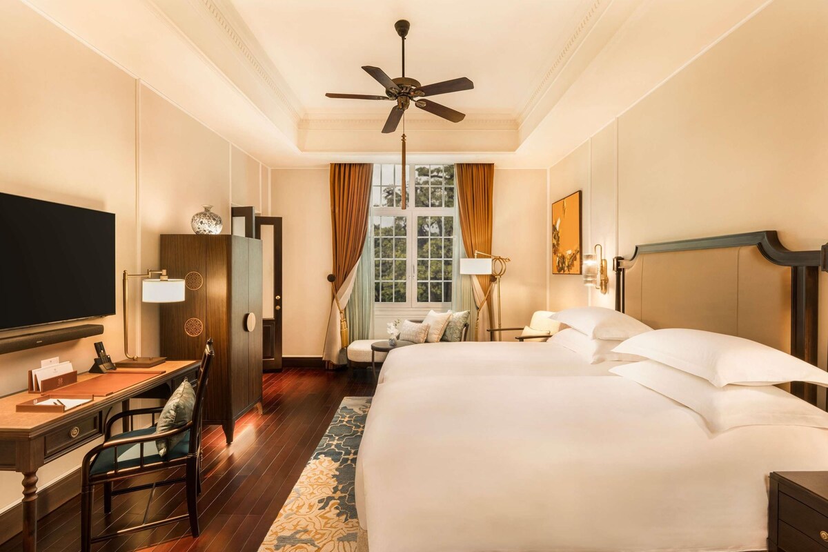 A hotel room with a bed, desk, chair, television, and a ceiling fan.