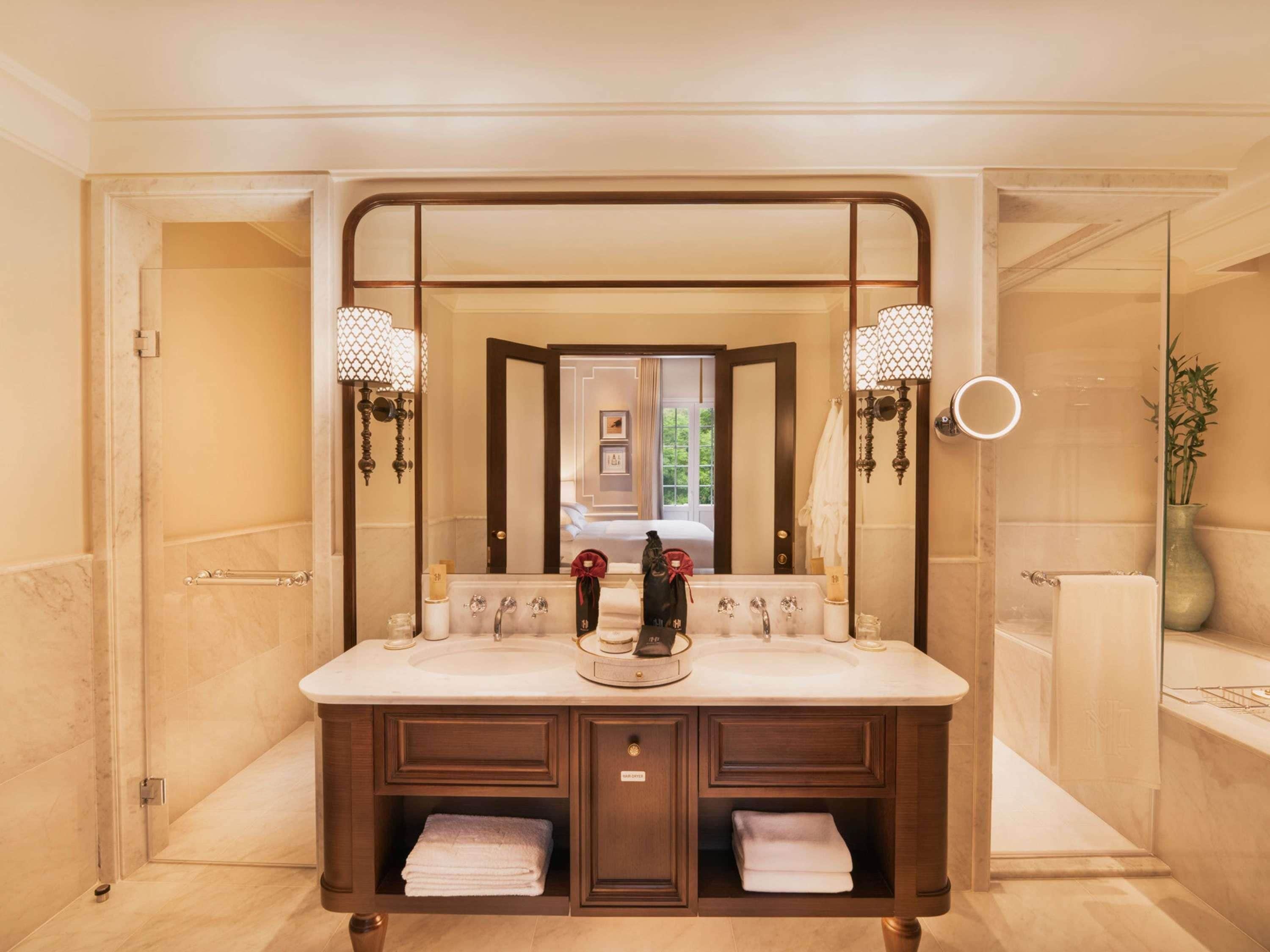 Une salle de bain avec un double lavabo, deux appliques murales, un miroir et un meuble-lavabo doté d’un porte-serviettes.