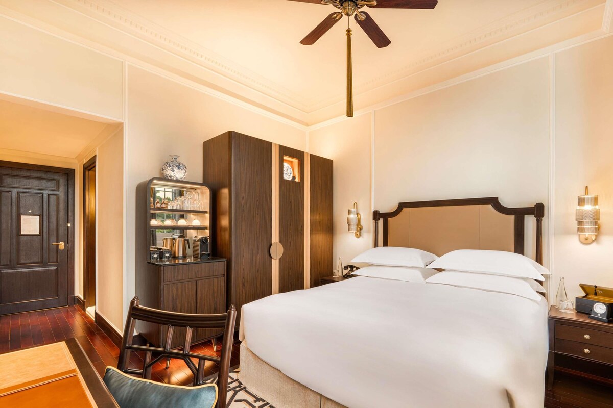 A hotel room with a bed, a desk, a wardrobe, and a ceiling fan.