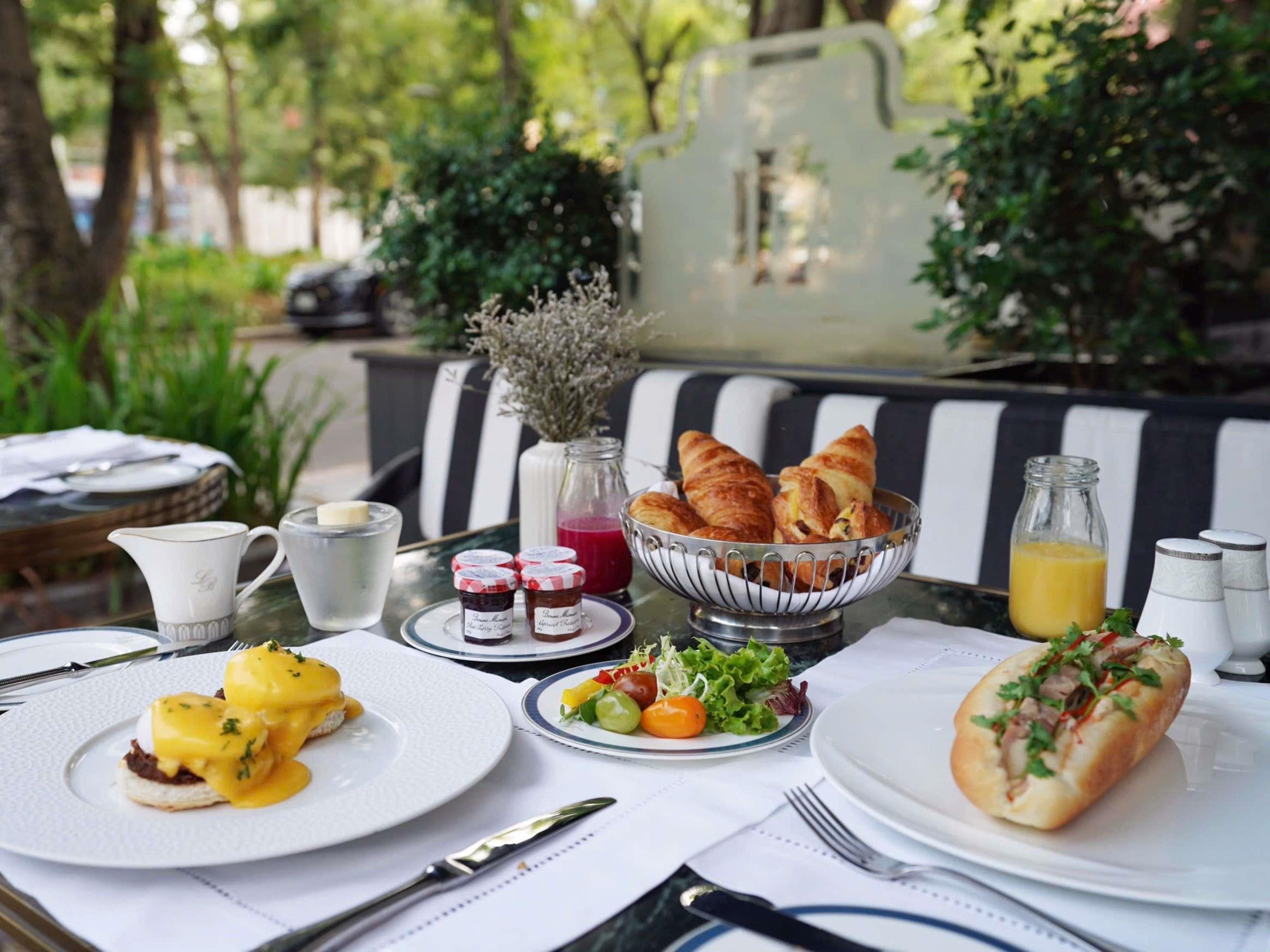 An outdoor dining setup with croissants, a salad, eggs Benedict, and a bottle of orange juice.