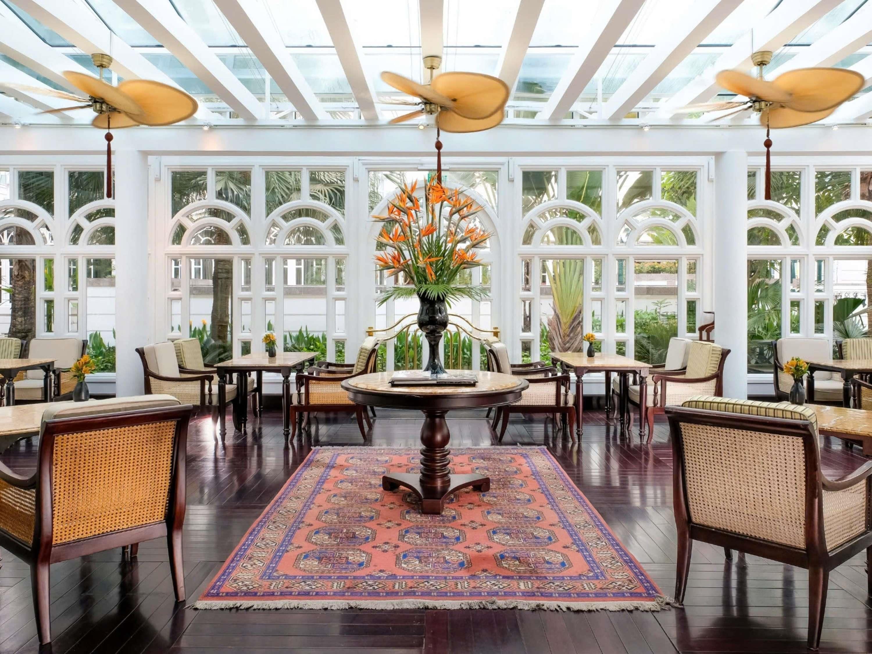 A spacious room with a high ceiling, large windows, and a central round table surrounded by chairs.