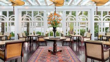 A spacious room with a high ceiling, large windows, and a central round table surrounded by chairs.