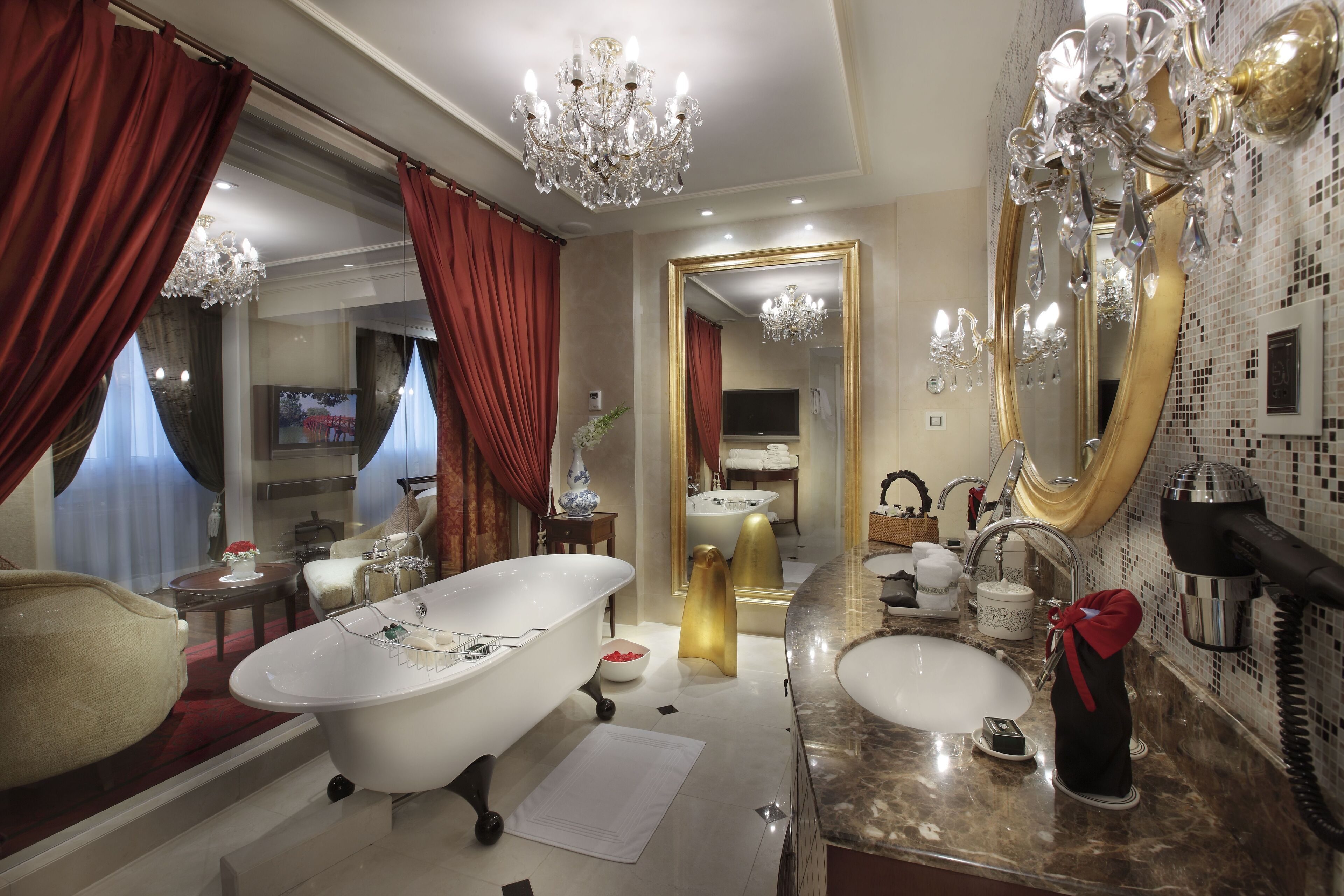 Ein luxuriöses Badezimmer mit einer freistehenden Badewanne, einem großzügigen Waschtisch mit goldener Spiegel und einem Chandelier.