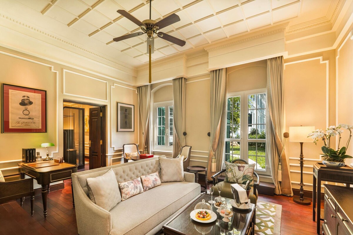 A well-appointed hotel room with a sofa, dining table, and a ceiling fan.
