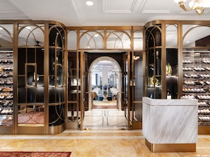 A luxurious wine cellar with a marble reception desk and a view into a dining area.