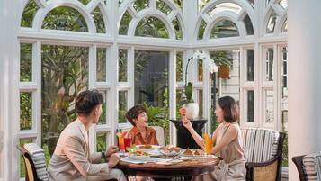 A dining area with a round table, white-framed windows, and wicker chairs.