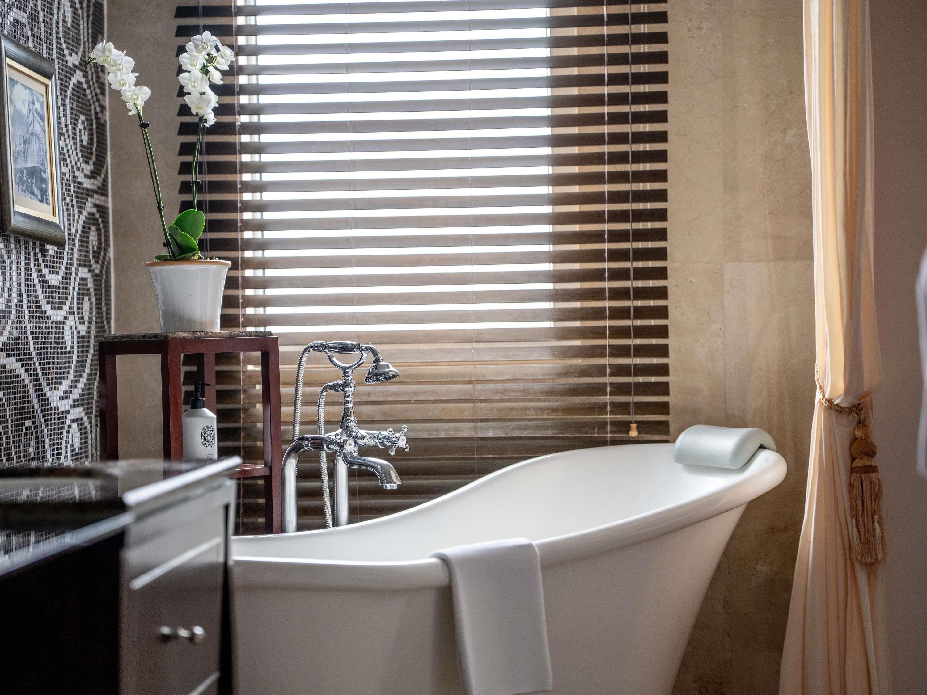A bathroom with a freestanding bathtub, a potted orchid, and a framed picture on the wall.