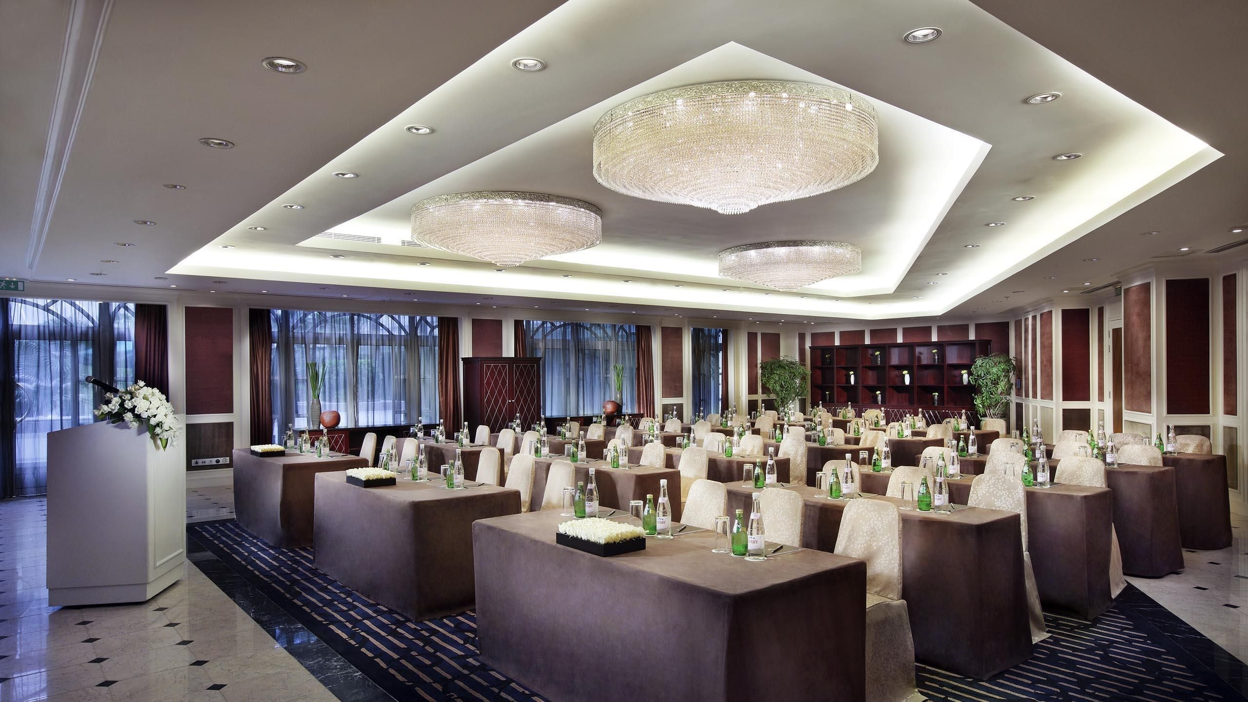 Een ruime vergaderzaal met meerdere tafels, elegante kroonluchters en een modern ontwerp.