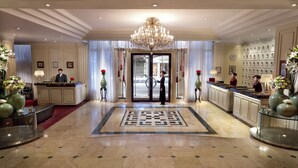 Eine Hotelhalle mit einem prächtigen Chandelier, einem Empfangstresen und einem gemusterten Teppich.