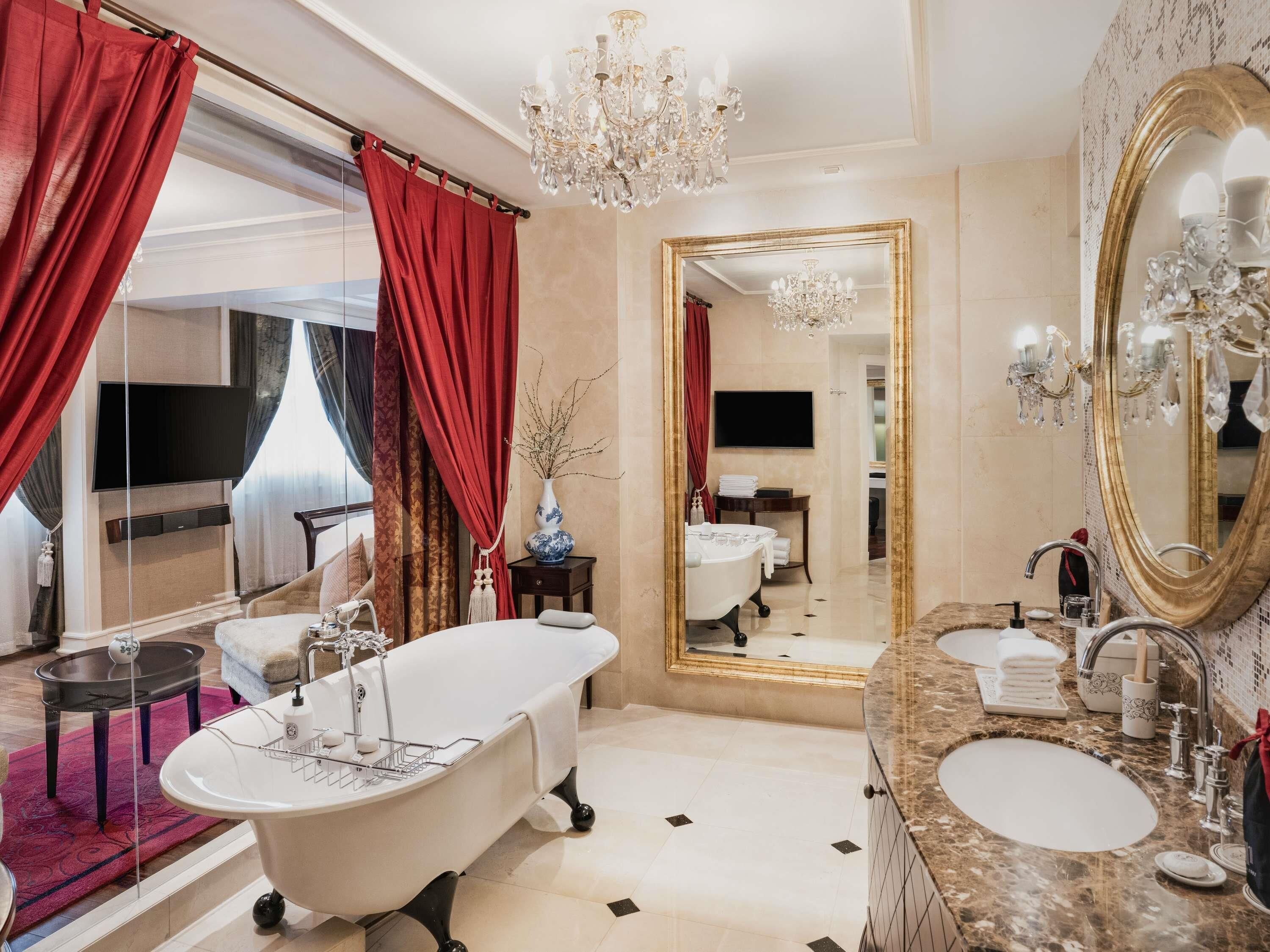 A luxurious bathroom with a freestanding bathtub, a large mirror, and a chandelier.