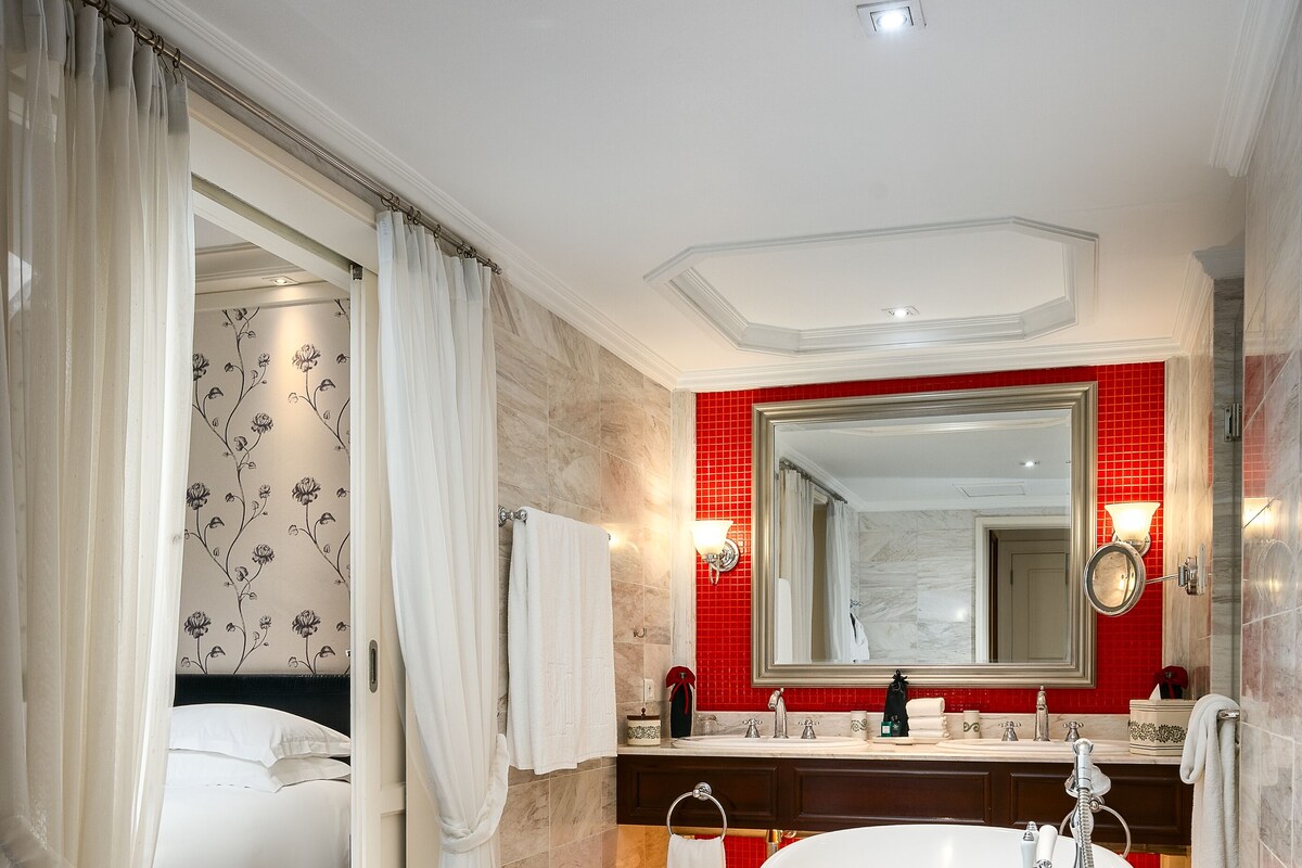 Ein Badezimmer mit freistehender Badewanne, einem großen Spiegel und einer Wand mit roten Fliesen.