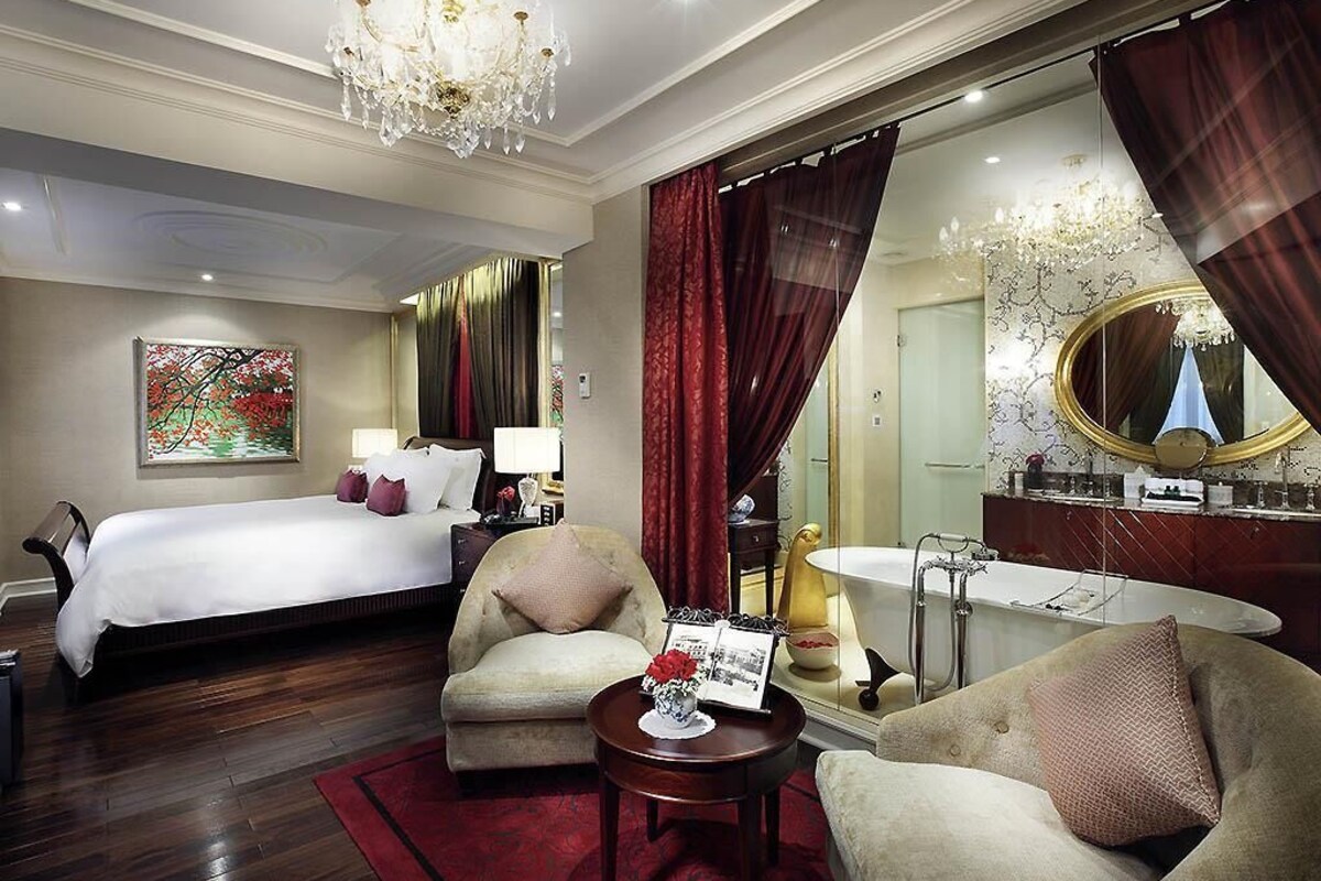 Ein Hotelzimmer mit einem großen Bett, einer Sitzecke inklusive Sofa und Sessel, einem runden Tisch, einem großen Spiegel und einer Badewanne.