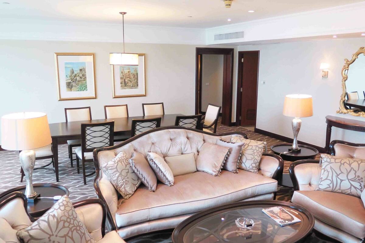 A hotel room with a plush sofa, a dining table with chairs, a coffee table, and two lamps.
