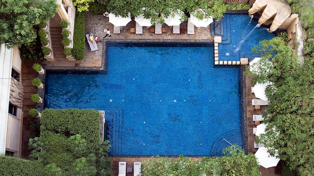 A large rectangular pool with a stone border, surrounded by white umbrellas and potted plants. - The Great Duke Phnom Penh (Phnom Penh)