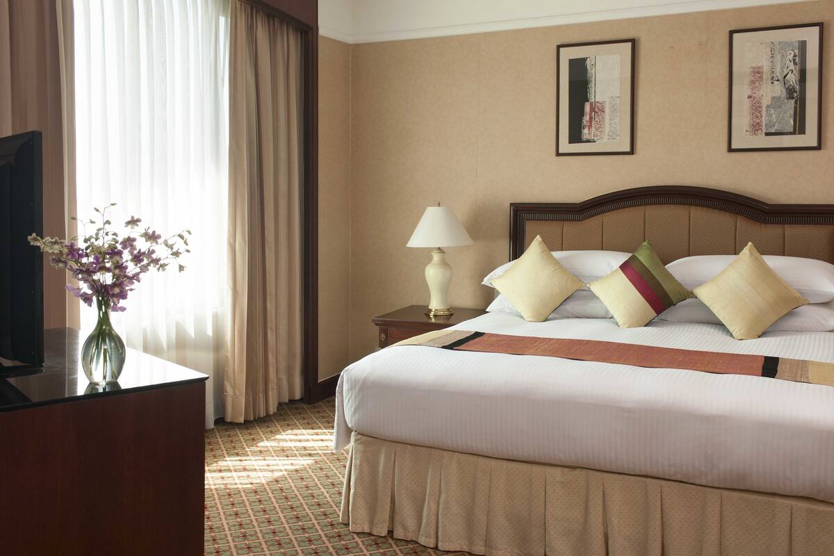 A hotel room with a bed, a nightstand, a lamp, a vase with flowers, and a television.